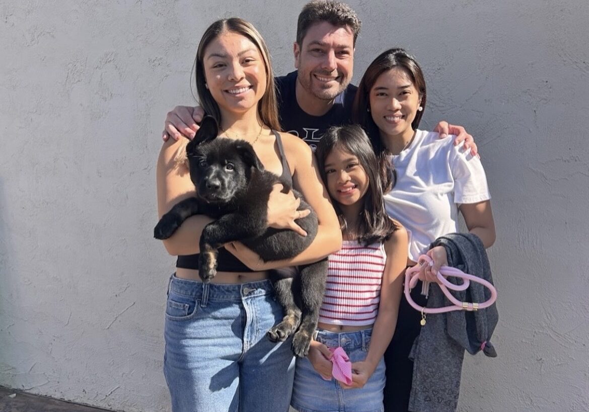 A happy family with two girls and a dog posing outside.